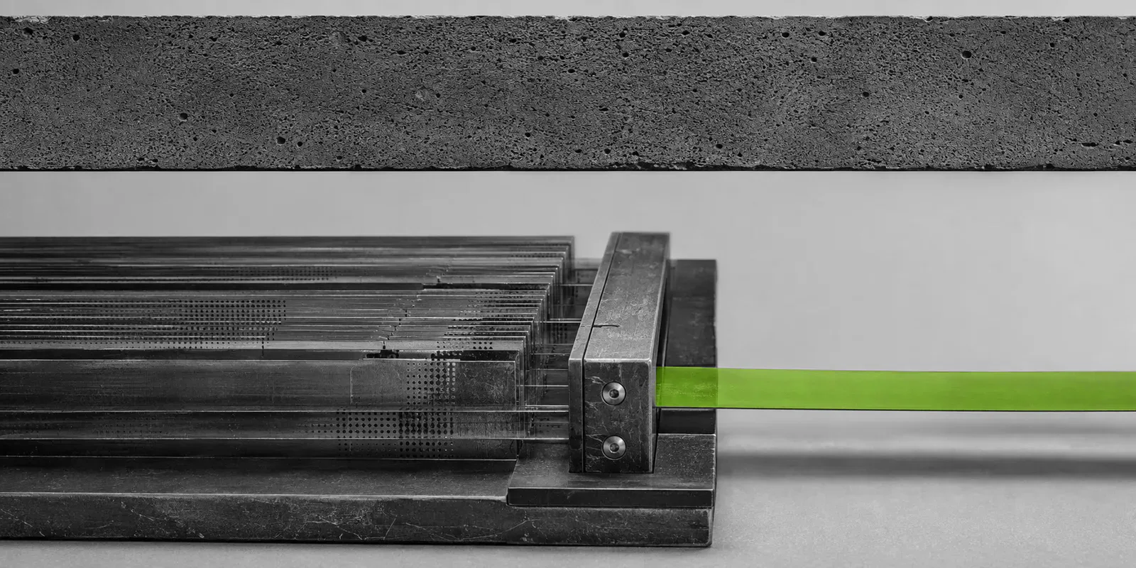 Un archivo de láminas de vidrio y metal atraviesa una compuerta y sale como una cinta verde bajo una viga horizontal de hormigón.