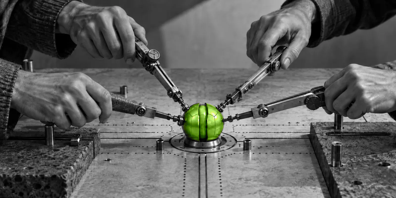 Cuatro manos coordinan brazos mecánicos que ensamblan en paralelo una esfera verde.