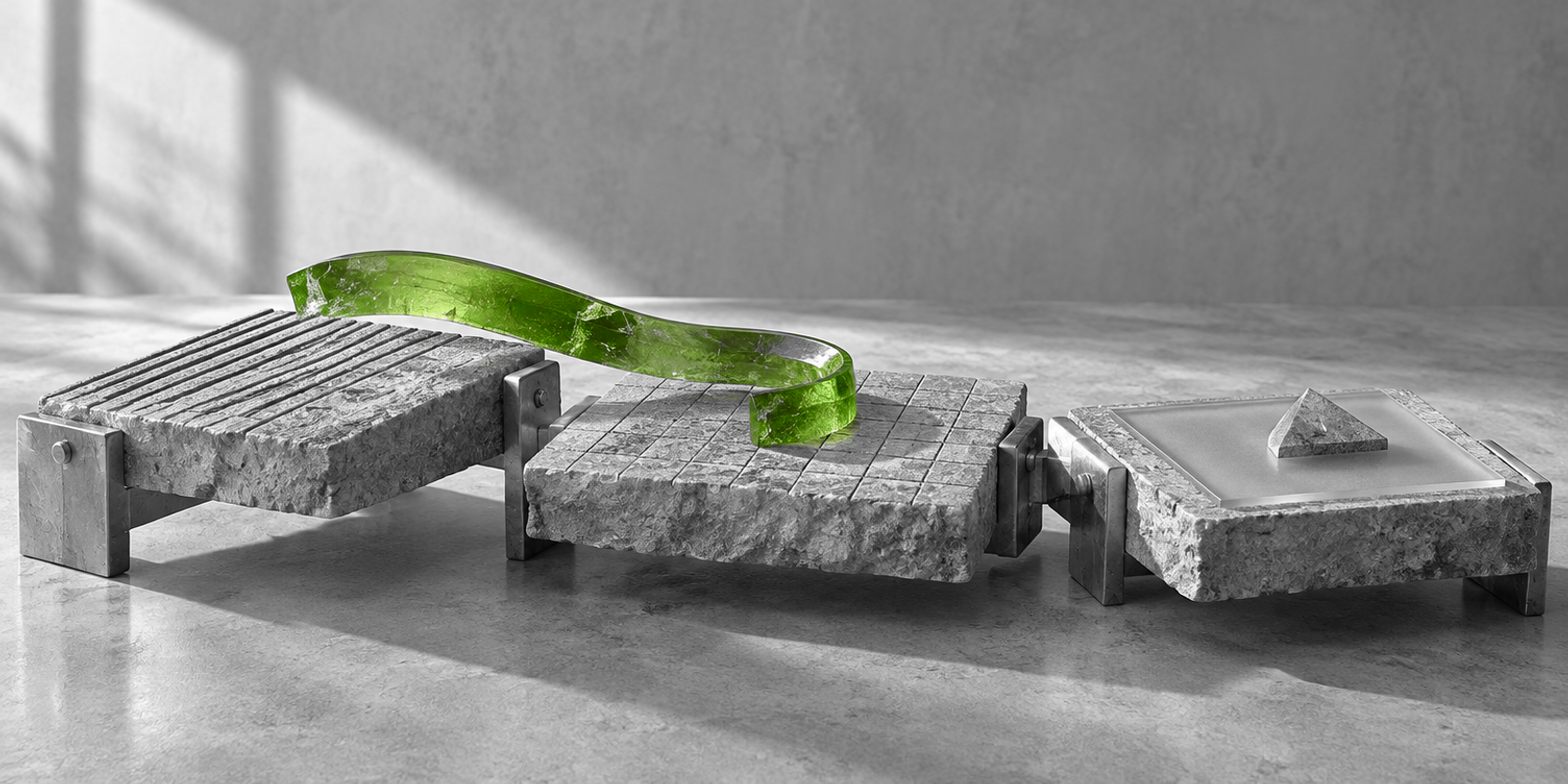 Tres planos de trabajo de piedra y metal quedan unidos por una cinta de vidrio verde que atraviesa sus juntas, sobre una mesa gris con marcas gráficas abstractas.